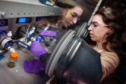 A woman holds a blue vial in a glove box. Her reflection looks back at her.