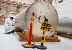 A man in a lab coat kneels besides a massive steel canister.