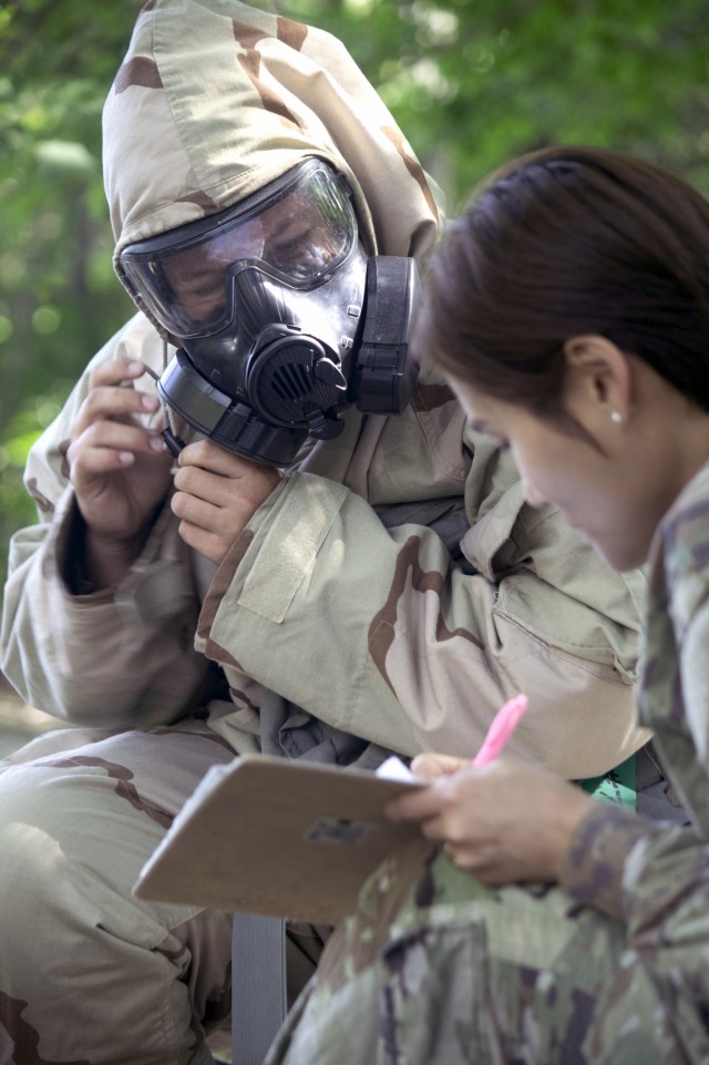 Cadet Rosalyn Page secures the hood of her protective hood over her gas mask as her cadre instructor, Spc. Ye Kim, 68th Chemical, Biological, Radiological, Nuclear, 2nd Battalion, Fort Cavazos, Texas, grades her proficiency on putting on Mission...