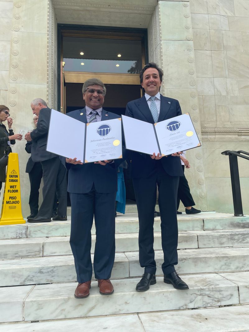 two men standing in front of building with certificates